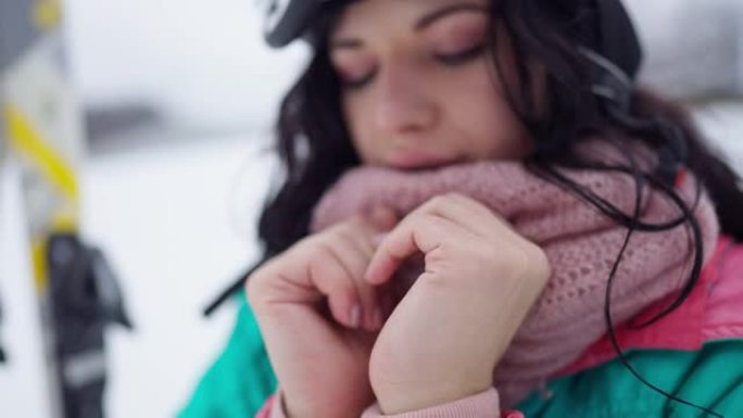 被冻结的女性苗条的手的特写镜头，背景是模糊的美女呼气。积极的年轻女性游客在户外冬季滑雪场休息。