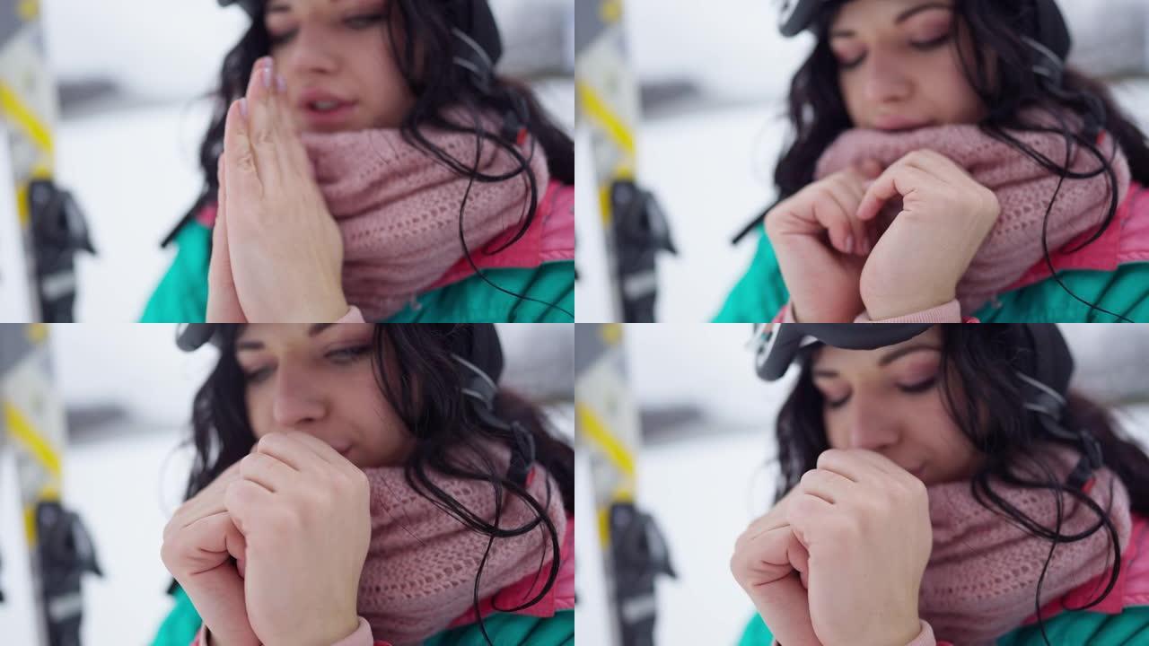 被冻结的女性苗条的手的特写镜头，背景是模糊的美女呼气。积极的年轻女性游客在户外冬季滑雪场休息。