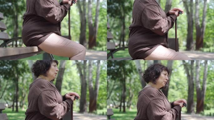 摄像机沿着坐在夏季公园长椅上的沮丧的高级妇女向上移动，叹气。沮丧的高加索退休人员在户外度过孤独的一天