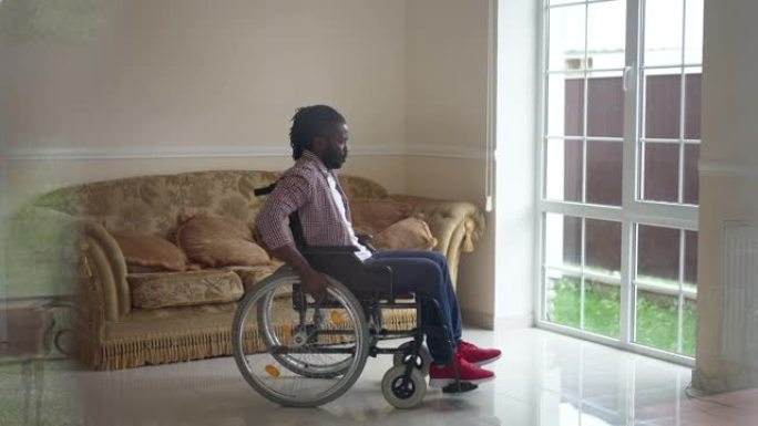 非洲裔美国残疾人以慢动作将手动轮椅滚动到门，看着窗外。大镜头侧视瘫痪在家里客厅的家伙。透过玻璃射击。