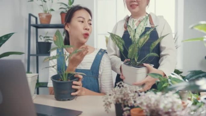 年轻的亚洲女性使用笔记本电脑接收采购订单，并在早上在树木商店通过相机在线展示植物录制视频。