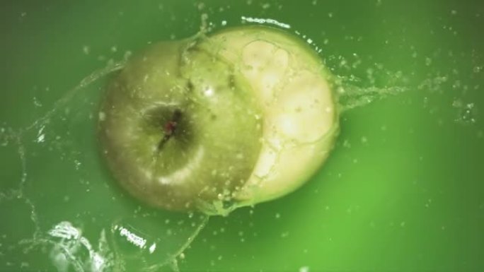 青苹果飞溅地落在果汁上，分成两半。
