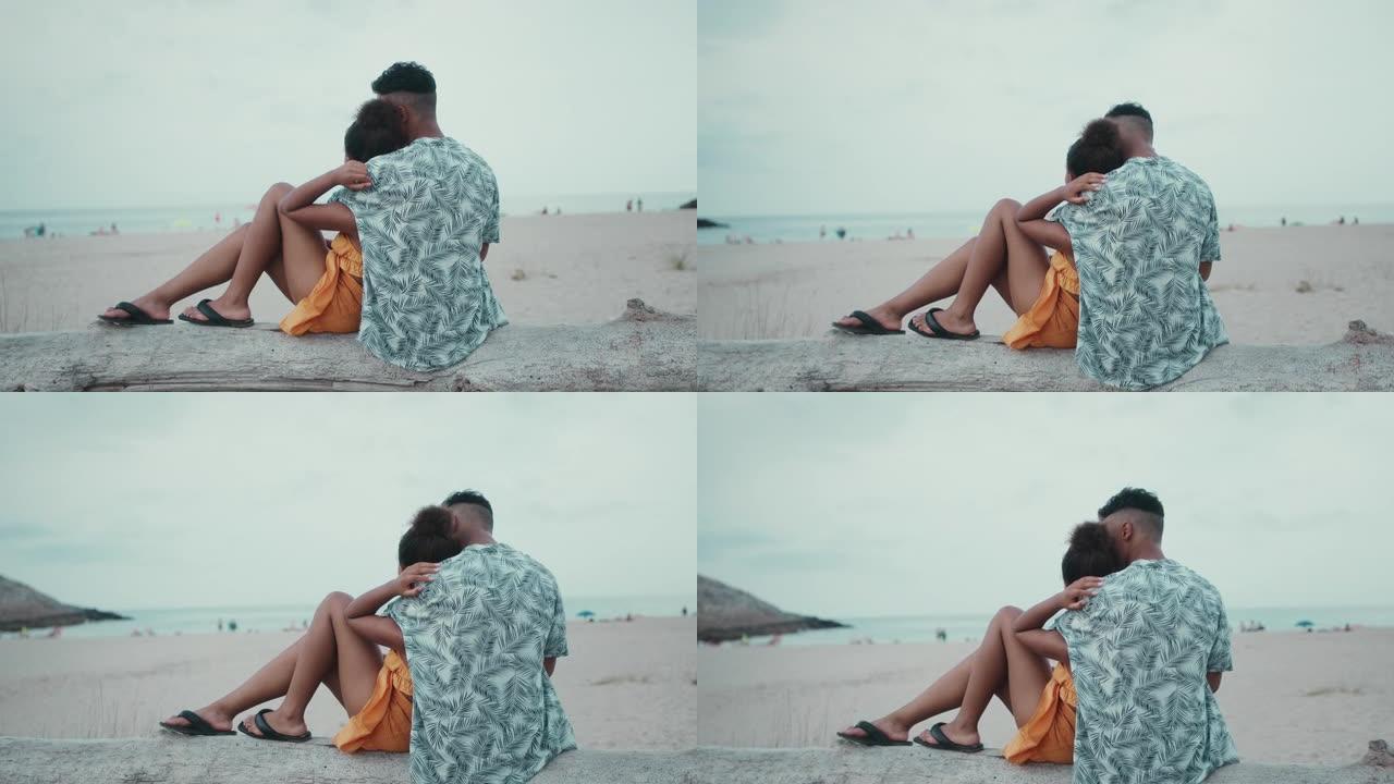 热爱非洲种族的夫妇坐在沙滩上，互相抱着。浪漫约会一起看海