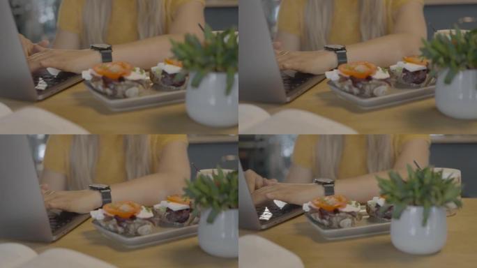 当年轻女子在笔记本电脑上工作时，在桌子上的咖啡馆餐的特写镜头
