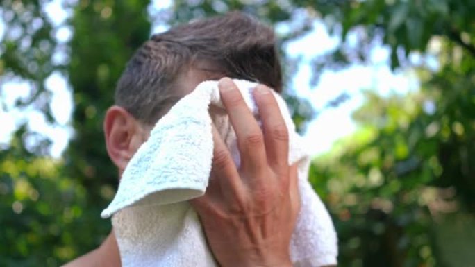 黑发高加索成年运动员的头像看着相机用白毛巾擦干脸上的汗水，然后移开目光。夏季锻炼后在后院摆姿势的健康