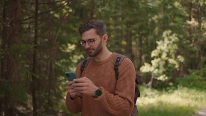 一个背着背包的男性旅行者沿着森林中的一条土路行走，写信息，在互联网上交流，查看内容。