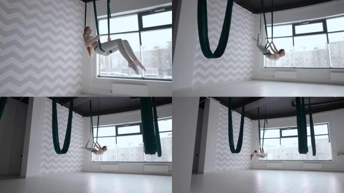 有吸引力的健身教练在绿色吊床上做反重力空中瑜伽练习。年轻灵活的女性在健身俱乐部练习航空伸展秋千。女性