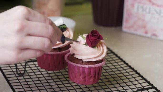 一个糕点厨师女孩用红玫瑰和糖球装饰纸杯蛋糕帽。