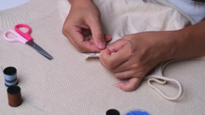 裁缝的手在用布料工作。母亲用手为她的小女儿缝了一件漂亮的衣服，特写镜头。女人用蓝线手工缝制接缝。