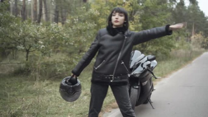紧张的年轻女子在空旷的道路上搭便车，破旧的摩托车站在后台。悲伤的高加索骑自行车的人在户外有摩托车问题