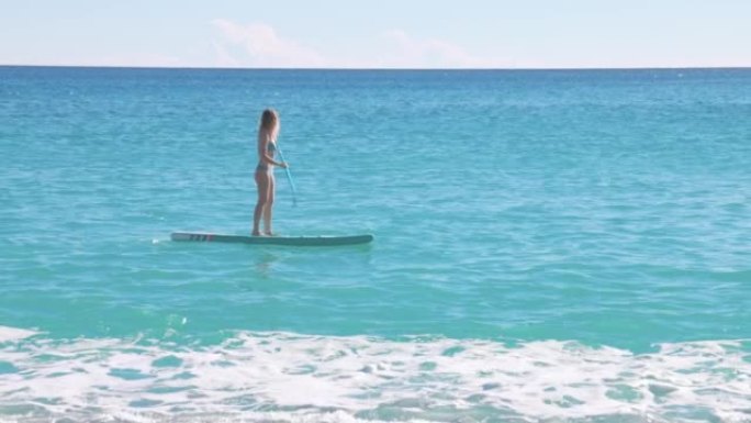 年轻的女飞行员在清澈的海水中站起来划桨板 (SUP)