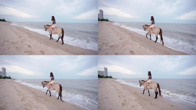 4K，一位年轻的亚洲妇女在太阳下山之前在沙滩上骑着马快乐地行走。游客来海滩放松，骑马，散步。