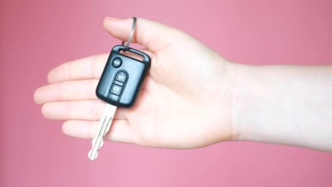 粉色背景上的女性手握车钥匙特写。