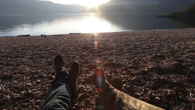 日落时在湖边海滩上放松的夫妇腿的细节