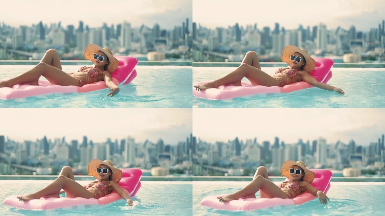年轻漂亮的性感女孩在游泳池里用粉色游泳床垫游泳