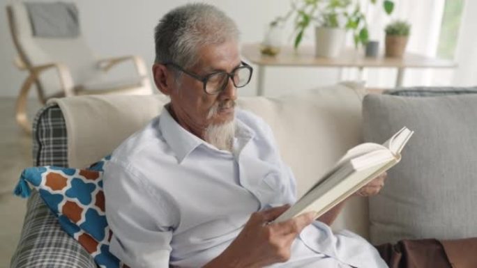 亚洲资深老人白发老人早上在家坐在沙发上看书，爱书人