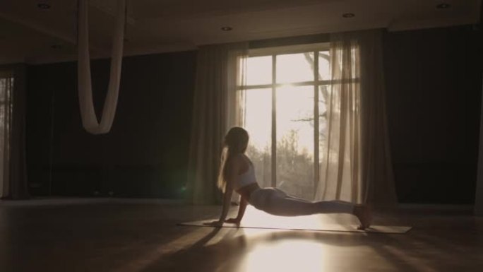 一名年轻女子在阳光下以慢动作练习瑜伽。透过窗户的光线，阳光