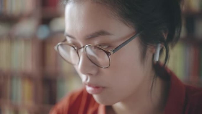 戴眼镜的亚洲妇女在笔记本电脑上工作，听在线课程