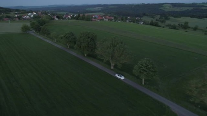空中无人机拍摄一辆白色跑车在日落时驶过山坡