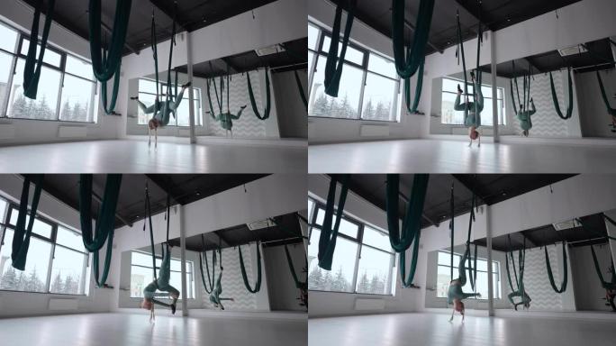 一个年轻漂亮的女人在空中瑜伽的吊床上练习。下午，一名妇女在大厅的镜子前独自表演伸展运动