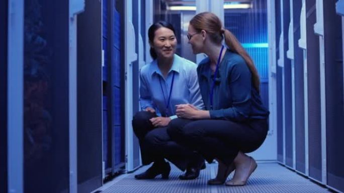 两名女性网络工程师蹲在服务器机房的服务器和检查操作