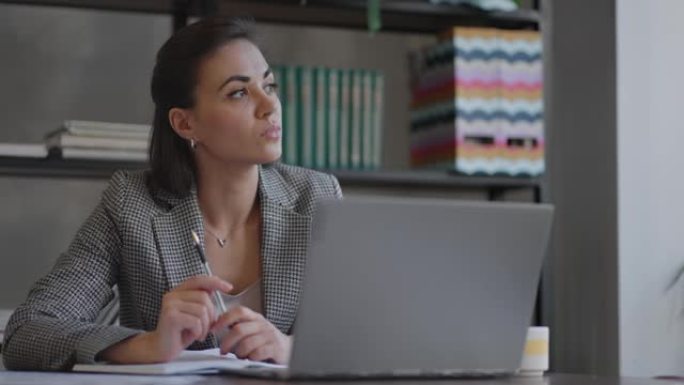 使用笔记本电脑坐在工作场所从事财务文书工作的阿拉伯西班牙裔妇女看起来很集中，同时使工作，准备，检查报