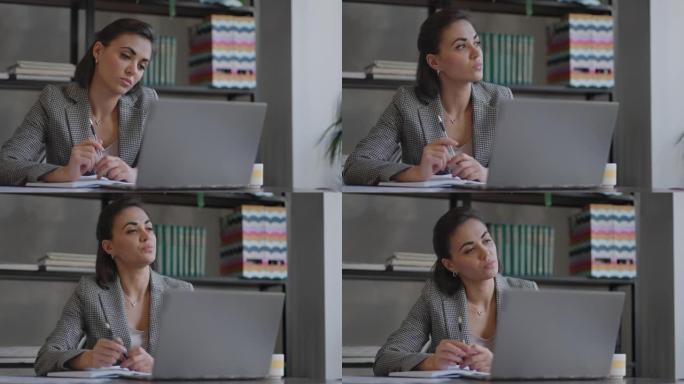 使用笔记本电脑坐在工作场所从事财务文书工作的阿拉伯西班牙裔妇女看起来很集中，同时使工作，准备，检查报