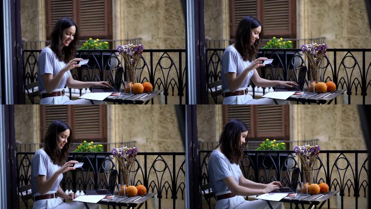 年轻女子坐在阳台上用笔记本电脑用信用卡在线购物