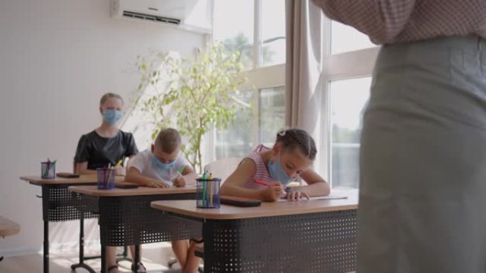 在学校，教室里，孩子们戴着防护面具在笔记本上写字，观察社交距离。大流行期间的学校教育