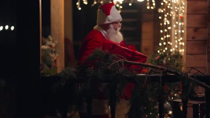 侧视图圣诞老人在冬天的街上手里拿着礼物，来到门口，带着花环和圣诞节装饰品进入房子