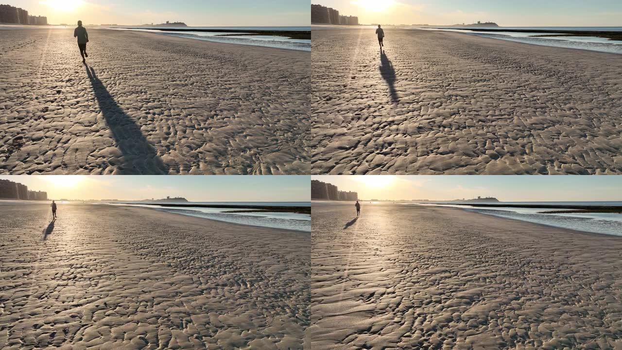 男子在空旷的海滩上奔跑的鸟瞰图
