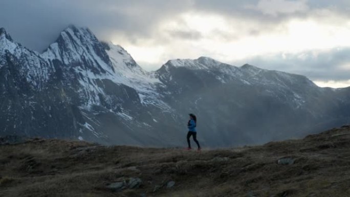 女子越野跑运动员在高山环境中奔跑，日落时分雪峰