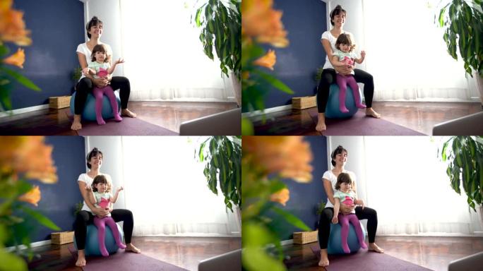 快乐的爱心妈妈和女儿在笔记本电脑上观看视频时在健身球上弹跳