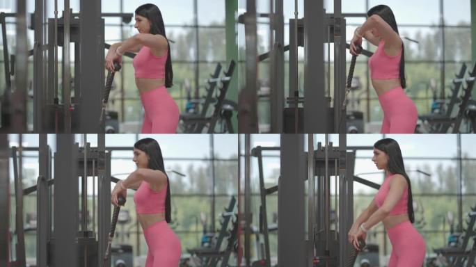 一位穿着粉红色西装的西班牙裔黑发妇女用手拉着一条交叉绳训练肩膀。教练的肩部锻炼。专业女性教练