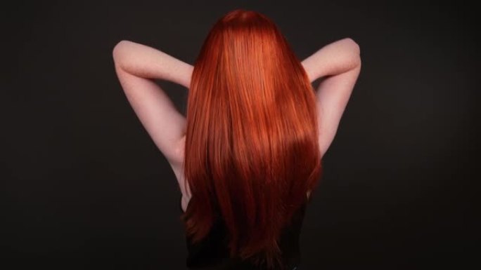 迷人的红发女人翻转她长长的直发。后视图