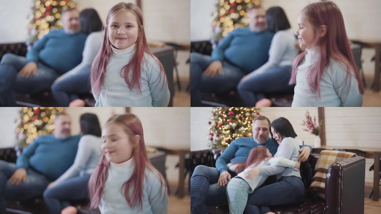 开朗的高加索女儿看着相机，跑回坐在背景沙发上的快乐父母。迷人的女孩在家享受圣诞假期庆祝。机架聚焦。