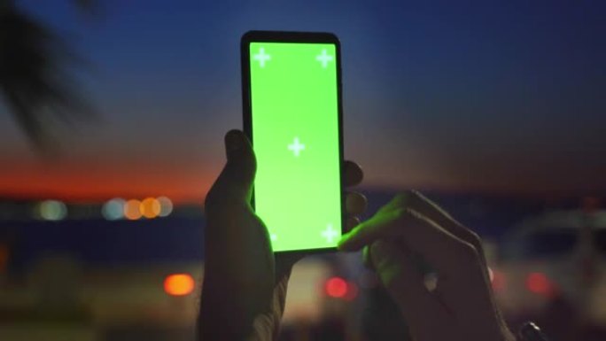 日落黄昏时用色度键绿色屏幕关闭智能手机，男性双手越过热带暮色，滚动浏览社交媒体或在线商店-互联网，通