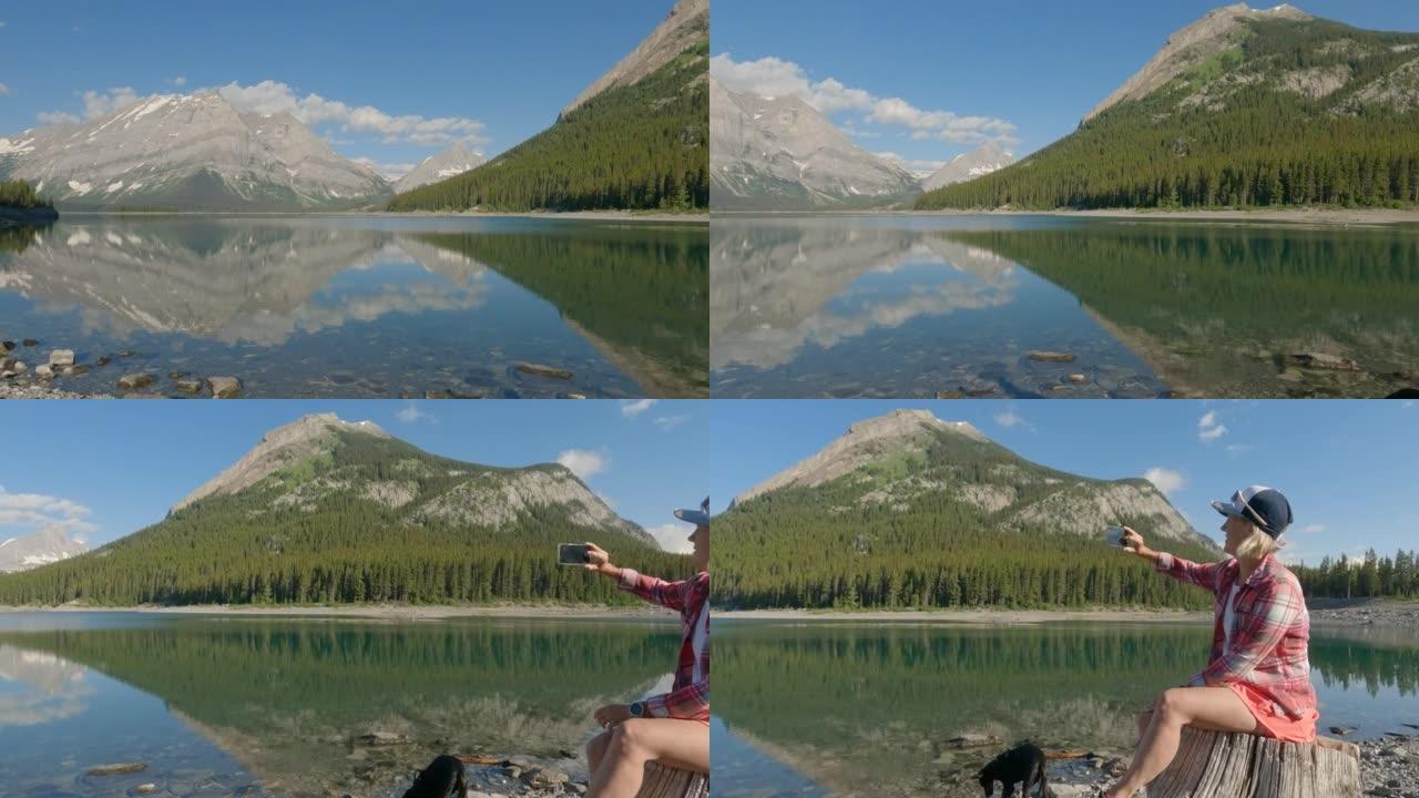 女人在山区湖岸享受时光，用智能手机拍照