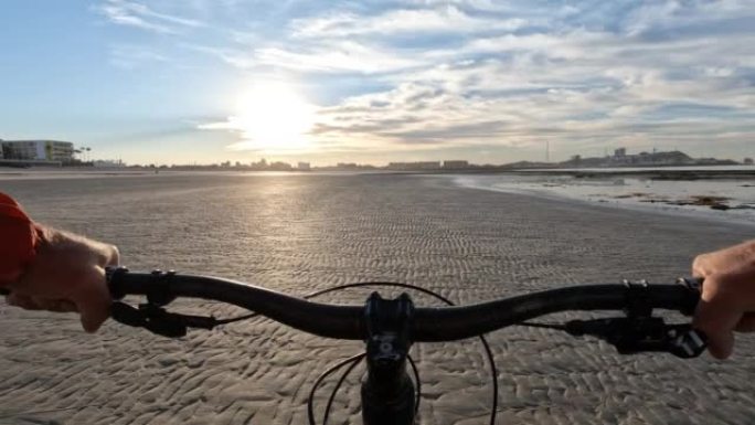 男子在空旷的海滩上骑自行车的第一人称视角