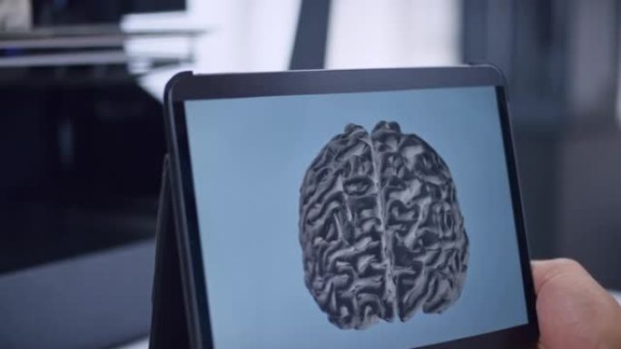 潘人拿着平板电脑，用大脑模型平面设计和3D打印机正在构建模型