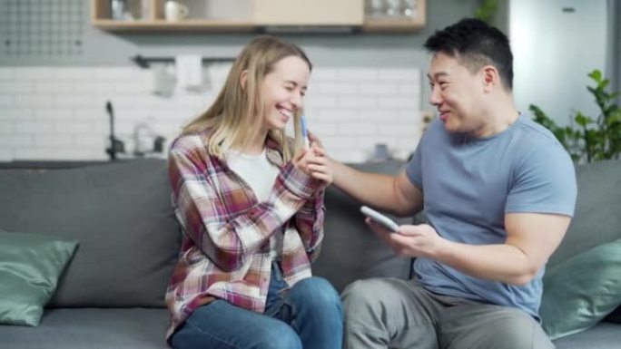 年轻的家庭享受积极的怀孕测试一对幸福的已婚夫妇亚洲男人和女人坐在沙发上拥抱和拥抱。