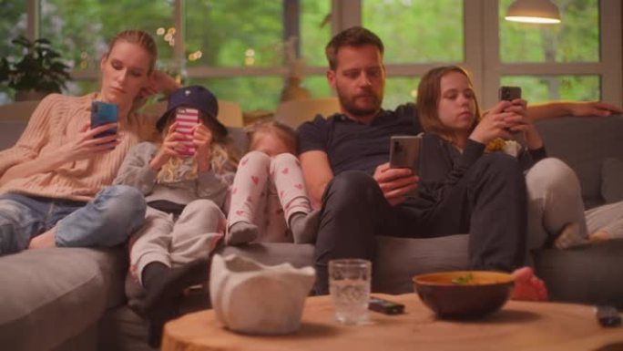 在家看电视。有三个女儿在一起的家庭。在沙发上使用智能手机