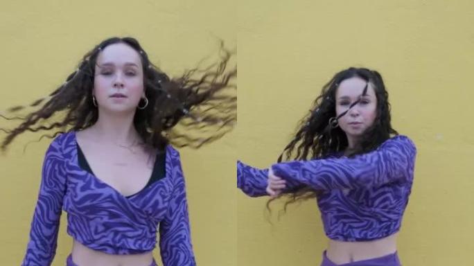 女嘻哈舞者在户外对着黄色墙壁跳舞时看着相机。