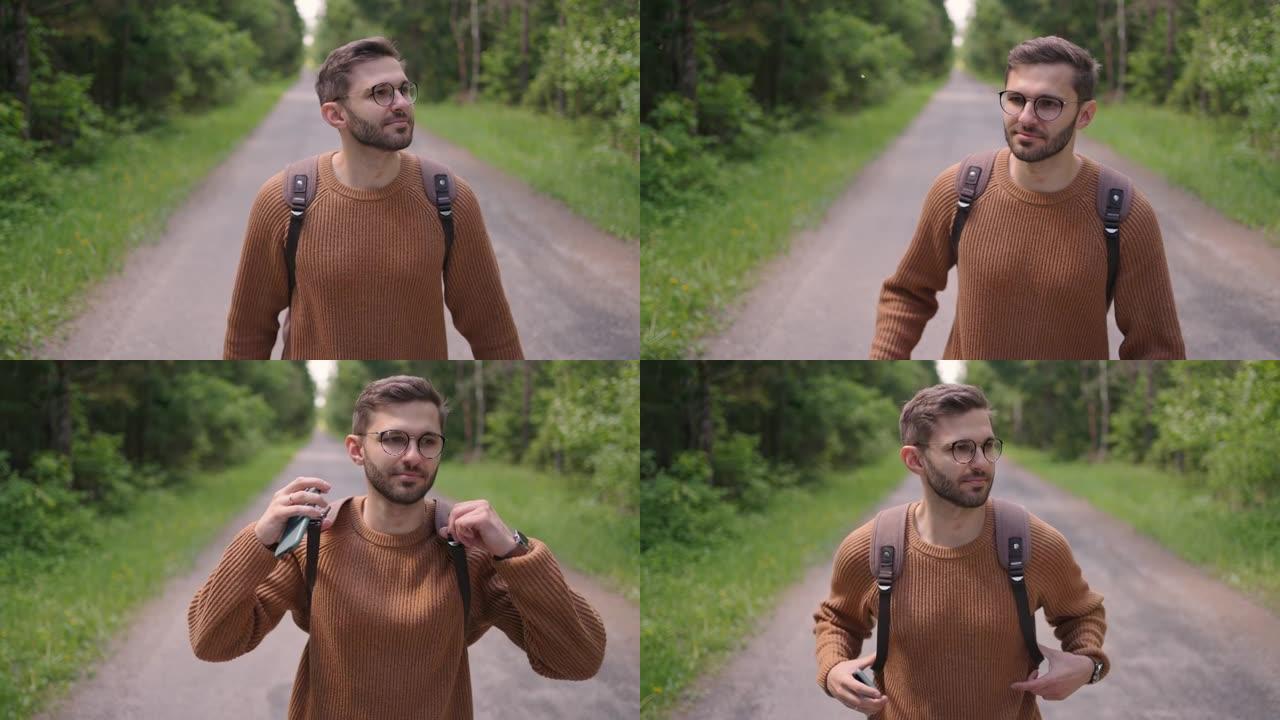 一个背着背包的年轻人正走在森林里的一条土路上，环顾四周的地形。前视图
