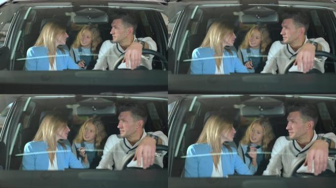 快乐的父母和坐在经销商的新车里的女儿交谈。积极的白人男人和女人在陈列室里和女孩一起选择汽车。家庭和消