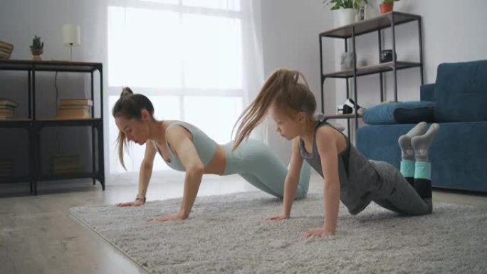 运动女人和她的小女儿正在家里做俯卧撑，家庭运动健康的生活方式，体育锻炼