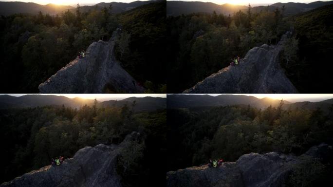 空中无人机拍摄的三名山地自行车手坐在日落时休息的岩石山脊上