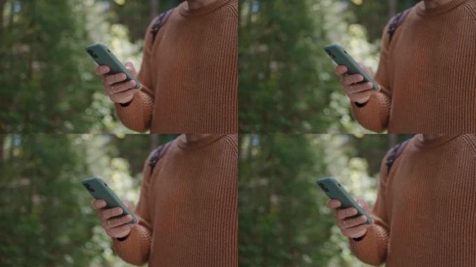 一个年轻人手中的手机在森林中旅行。导航器、信使和社交网络。使用手机搜索信息，在森林地区散步。