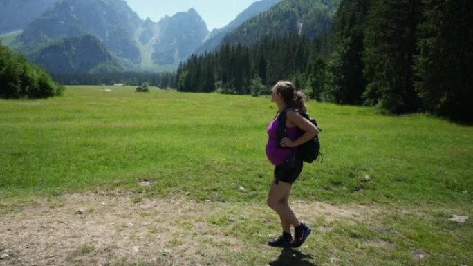 孕妇在山上徒步旅行，微笑着看着郁郁葱葱的绿色草地和落基山脉的景色