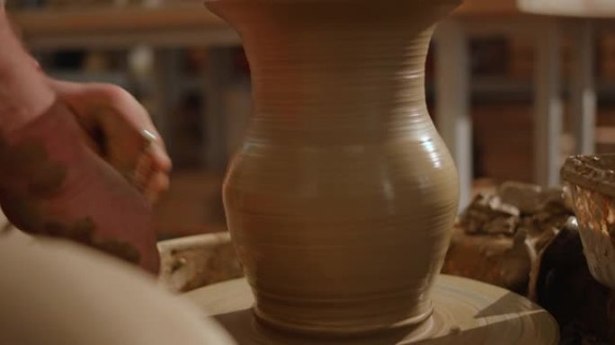 男性陶工的手准备将花瓶的底部从轮子上抬起